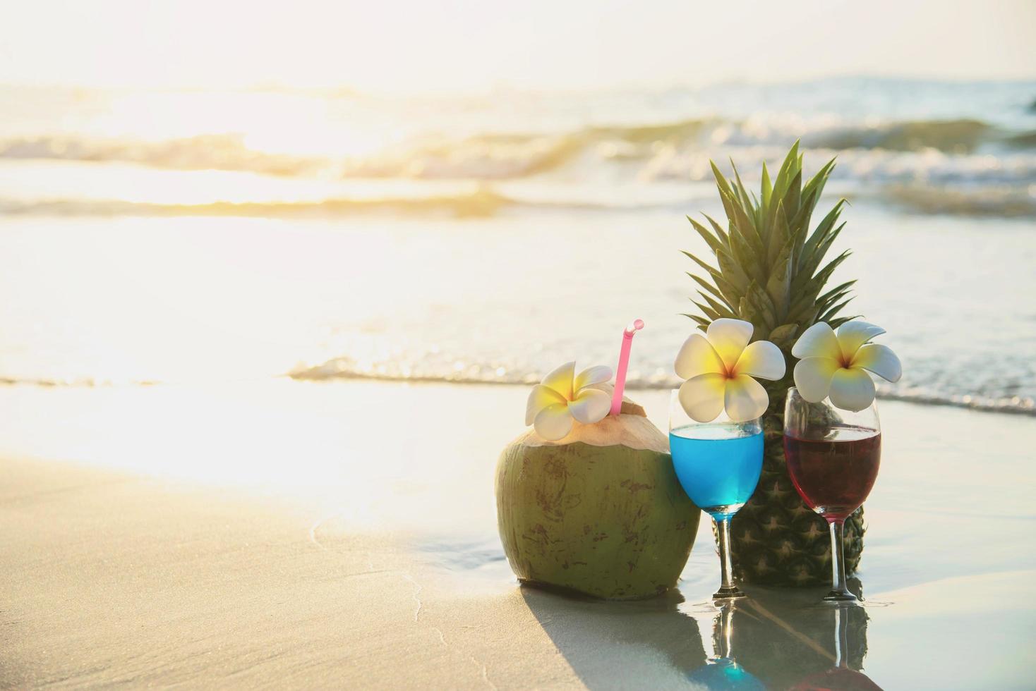 Cocktail glasses with coconut and pineapple on clean sand beach - fruit and drink on sea beach backgroudn concept photo