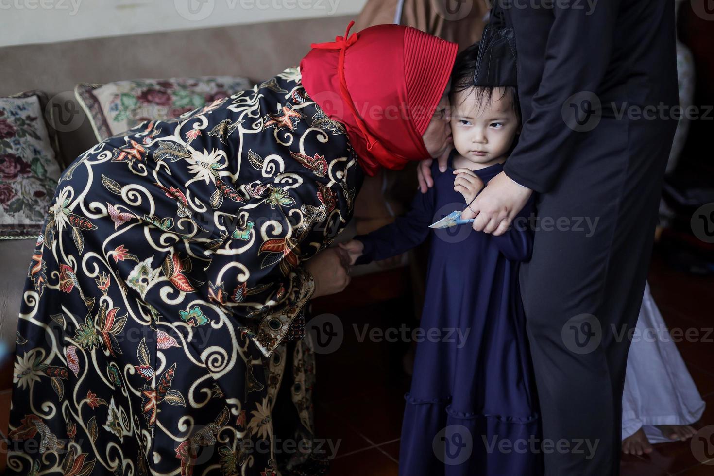 Grandmother kissing granddaughter's cheek during lebaran idul fitri day. photo