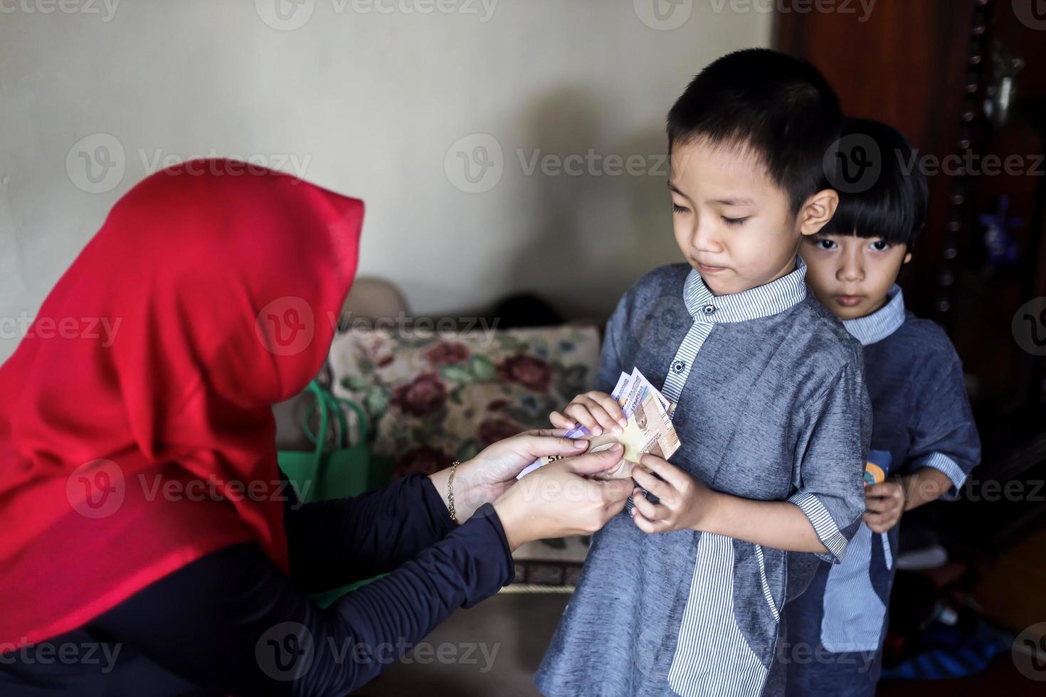 tradición del pueblo indonesio durante la celebración de eid mubarak de distribuir dinero o llamada thr. mujer musulmana asiática da dinero a un lindo niño de familia durante idul fitri. foto