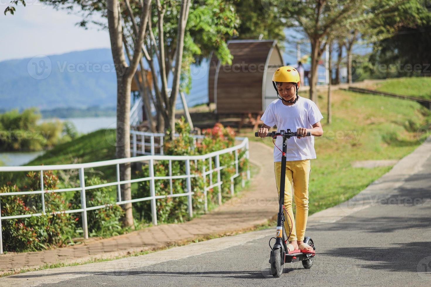 Portrait of  little Asian boy wear helmet enjoy having fun riding electric scooter at street park outdoors on sunny day. Healthy sport children activities outside. photo