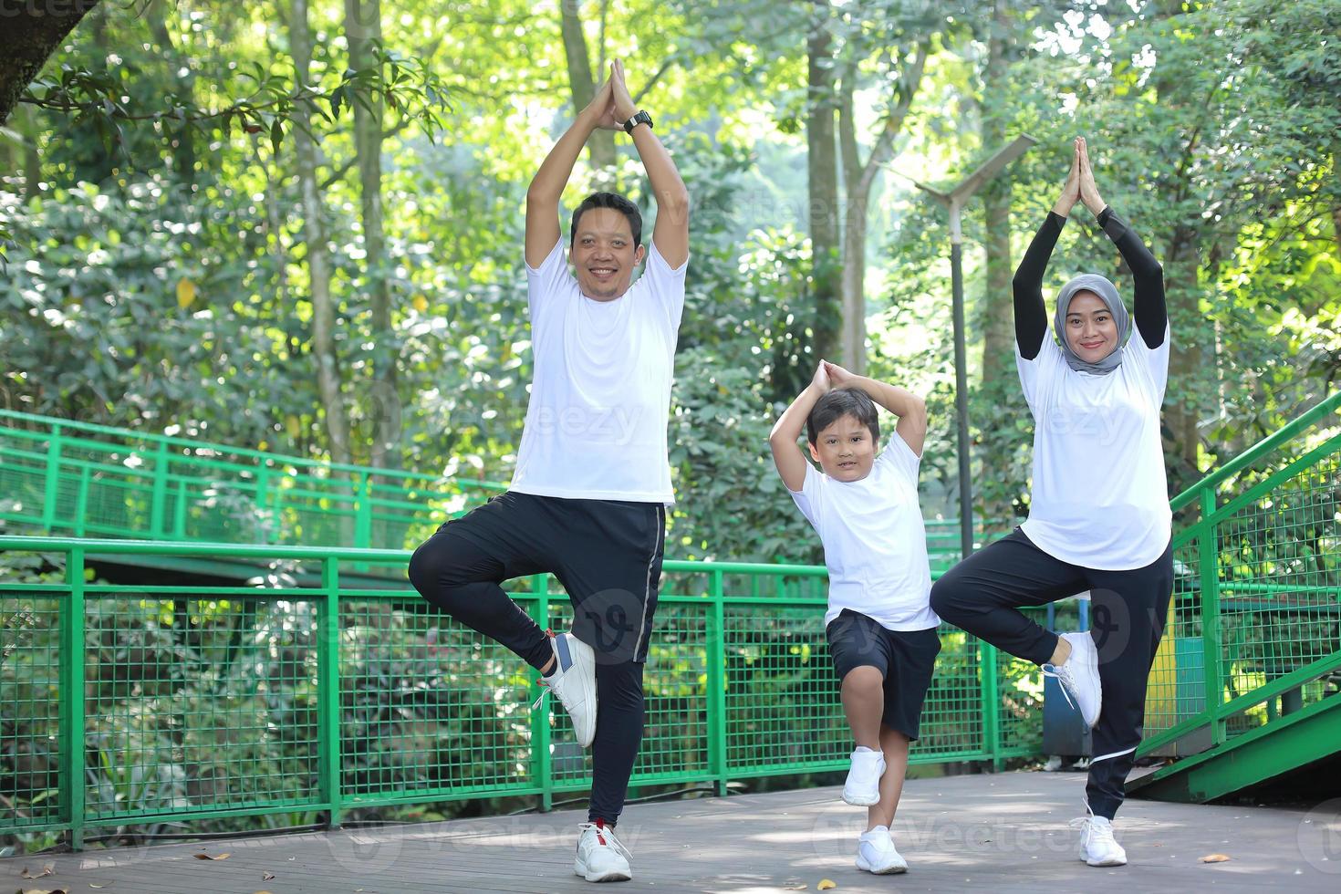 joven madre y padre asiáticos equilibrando el cuerpo y meditando yoga energético junto con su hijo en el parque verde. foto