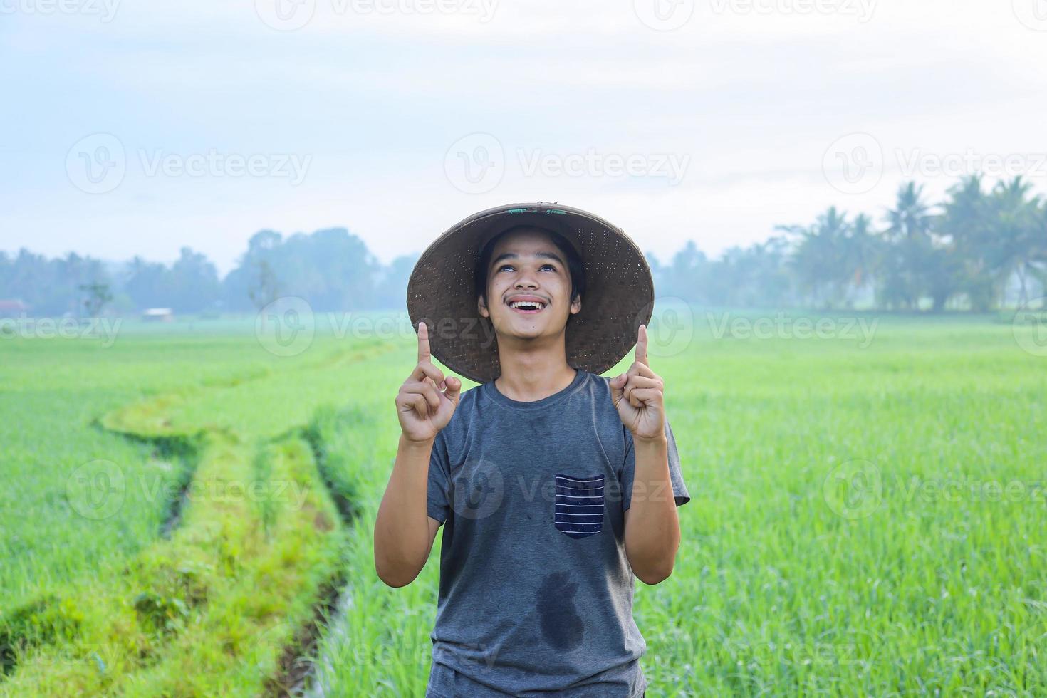 Portrait of attractive cheerful young Asian farmer standing and showing aha moment getting idea the rice field. Modern agriculture concept. photo