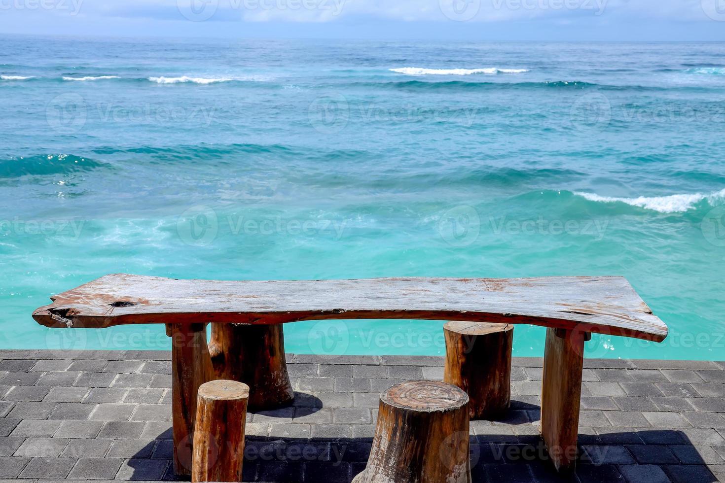 silla y mesa de madera junto al mar con un hermoso paisaje turquesa bajo el cielo azul. foto