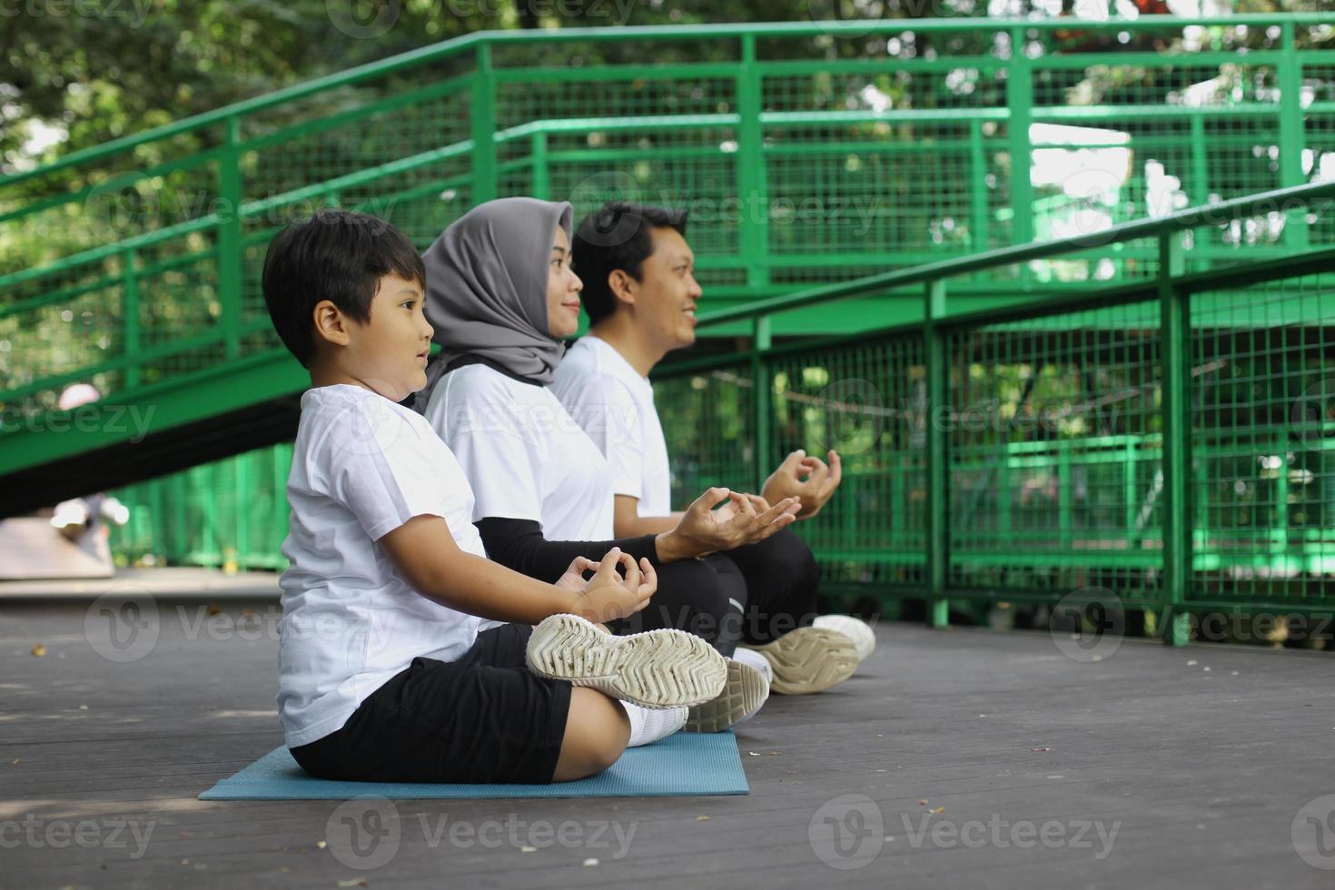 Young Asian family doing exercise in meditate yoga pose together at the greenery park. Healthy lifestyle family concept. photo