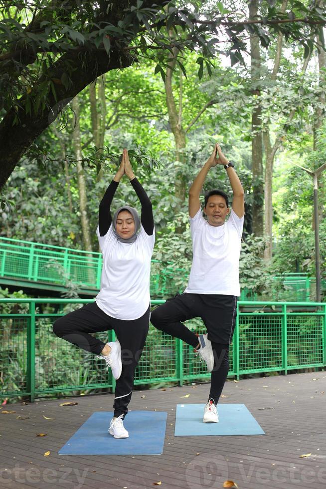 Young Asian couple balancing body and meditating energy yoga together at greenery park. photo