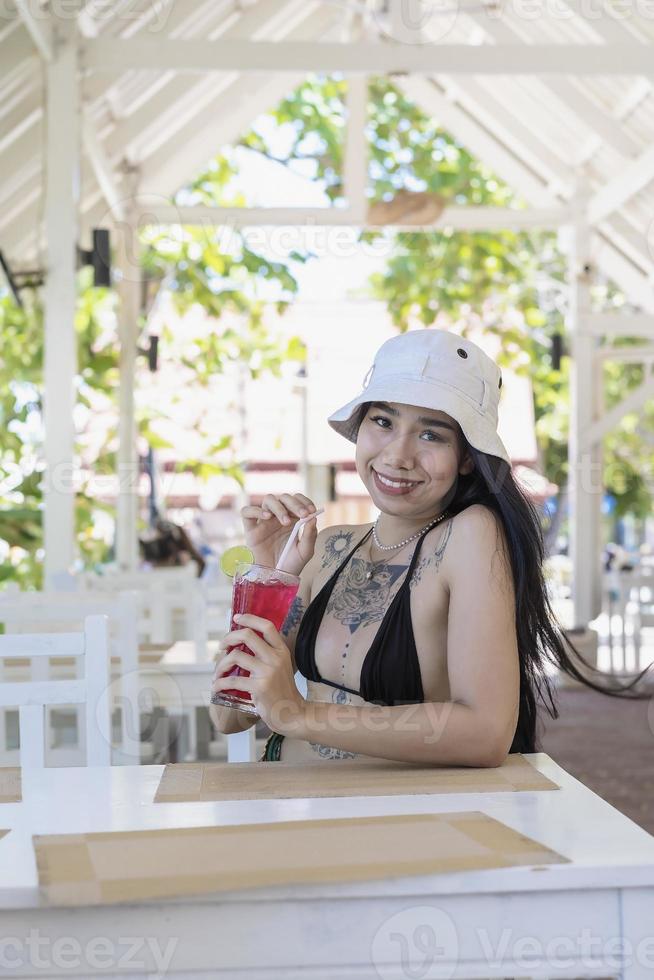 Youn beautiful and sexy Woman in Bikini with fresh juice in restaurant, smiling with happiness on vacation in summertime. Pretty smiling girl drinking tasty sweet red cocktail, amazing relaxing day photo