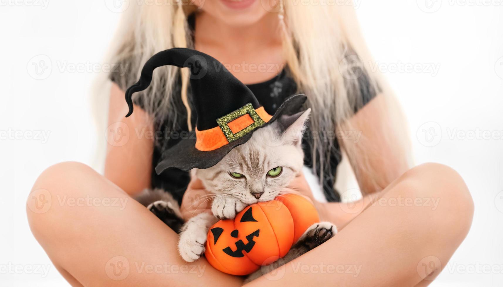 Disgruntled cat in the halloween costume with toy pumpkin in the arms of a girl photo