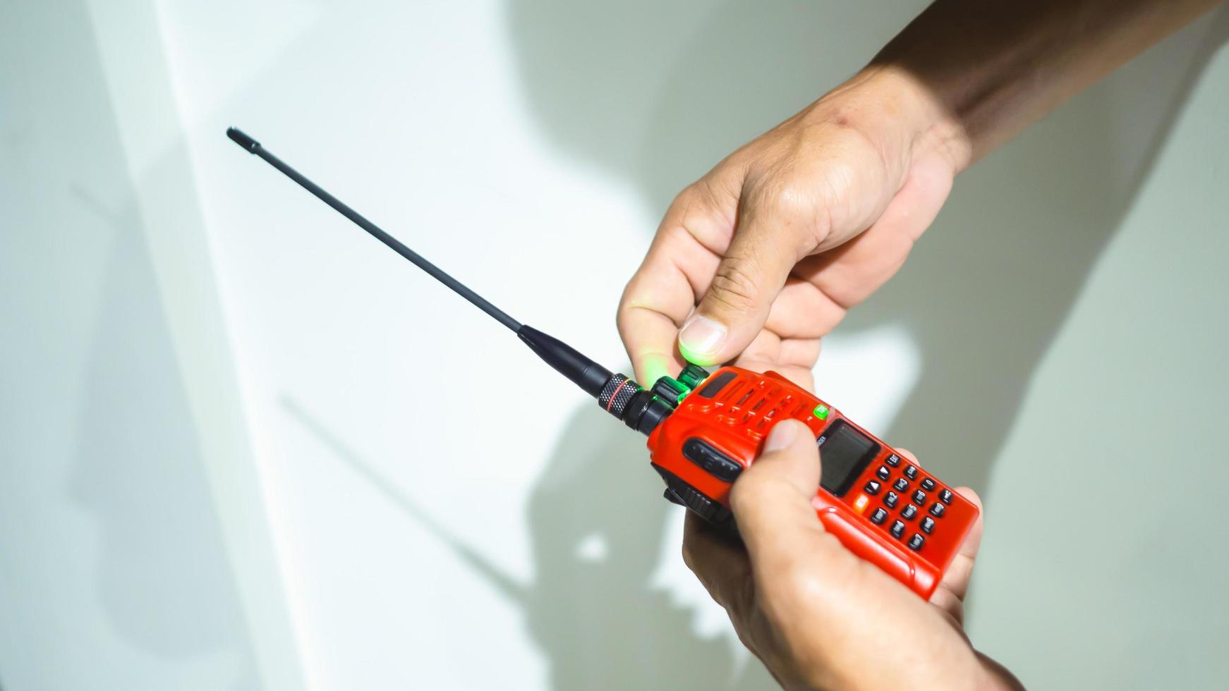 mano que sostiene la radio amateur roja, la otra mano gira el botón de la radio para configurar el uso. foto