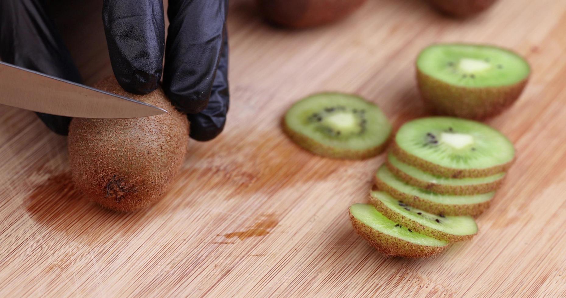 hold the kiwi with a black glove and cut it into thin slices photo