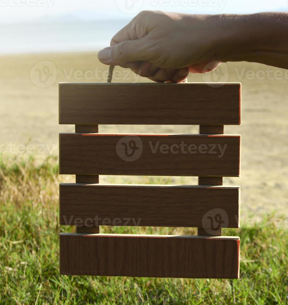 manos sosteniendo un marco de madera con un fondo borroso de hierba verde y océano. foto