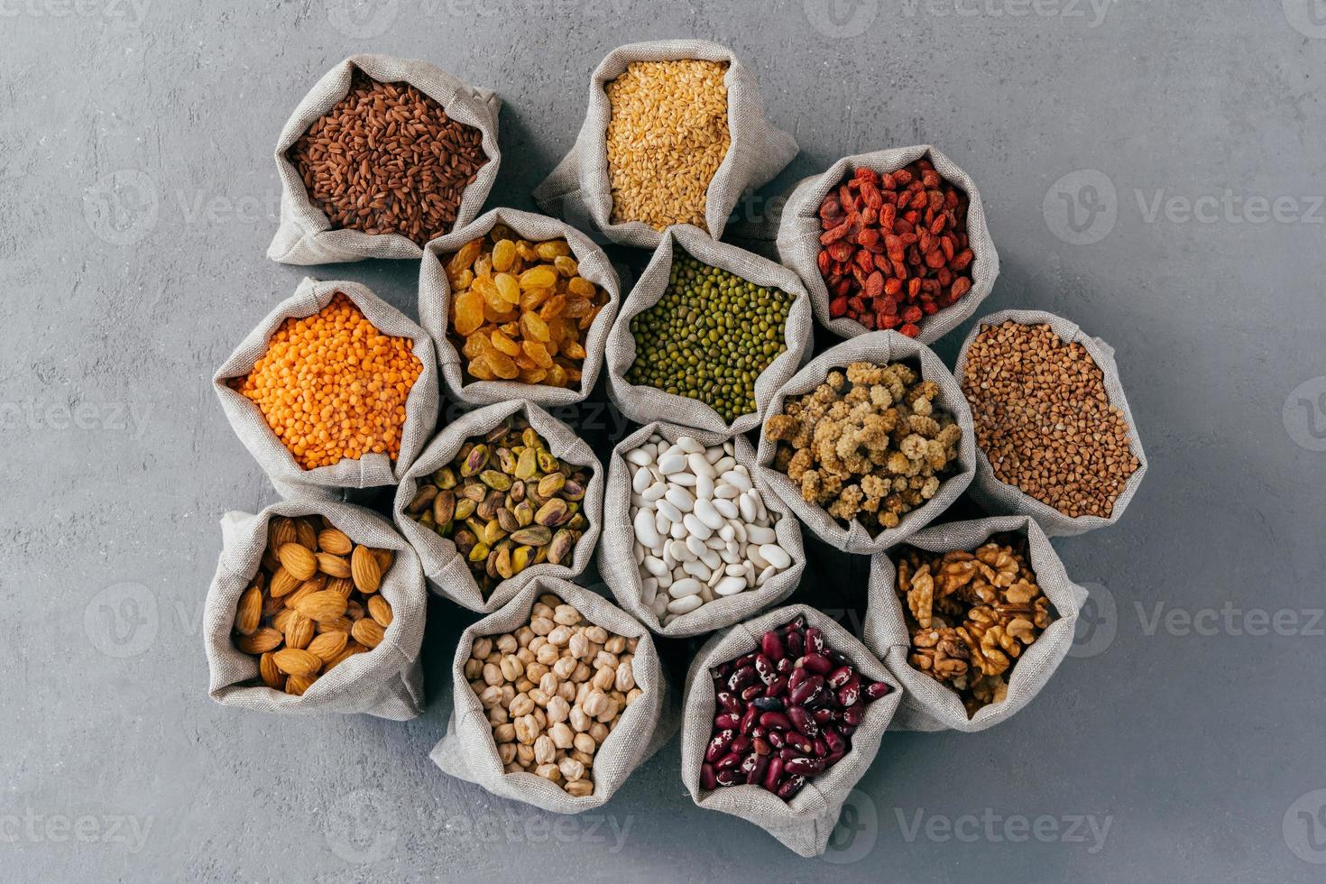 Natural cereal food concept. Top view of little cloth sacks stand around, consisted of healthy dried fruit and cereals. Mixed variety. Flat lay photo