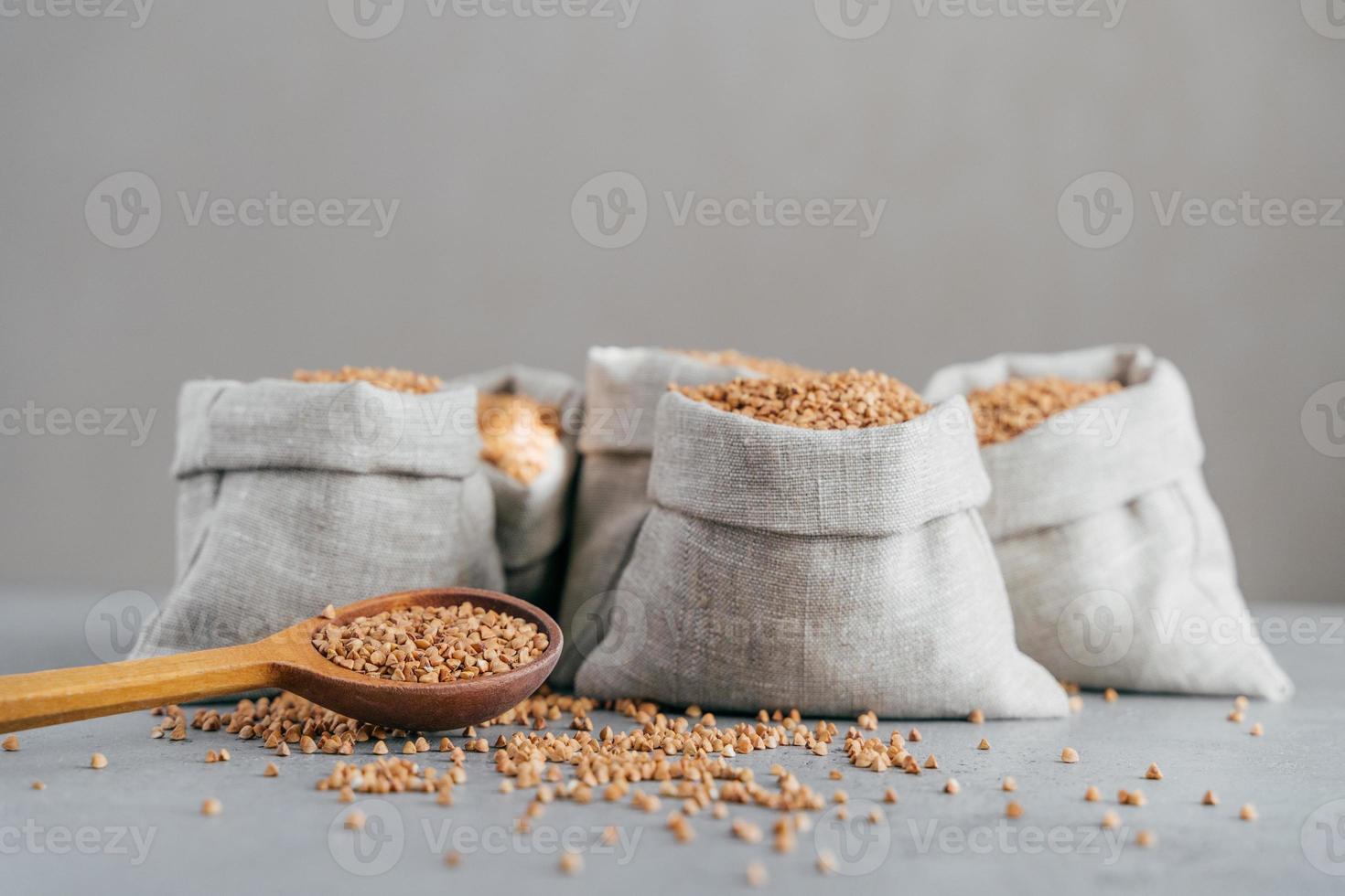 Eco food and dieting concept. Healthy brown buckwheat in bags and wooden spoon, isolated over grey background. Buckwheat kernels photo