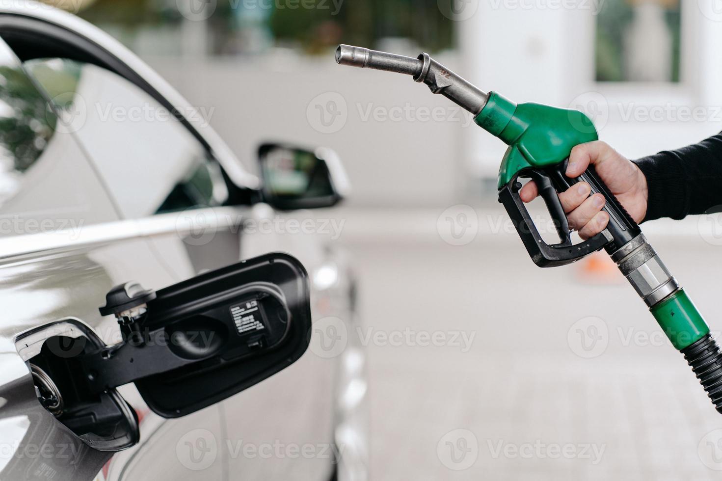 Cropped shot of mans hand pumping gasoline fuel in car at gas station. Auto being filled with petrol. Unrecognizable man holds fuel nozzel. photo