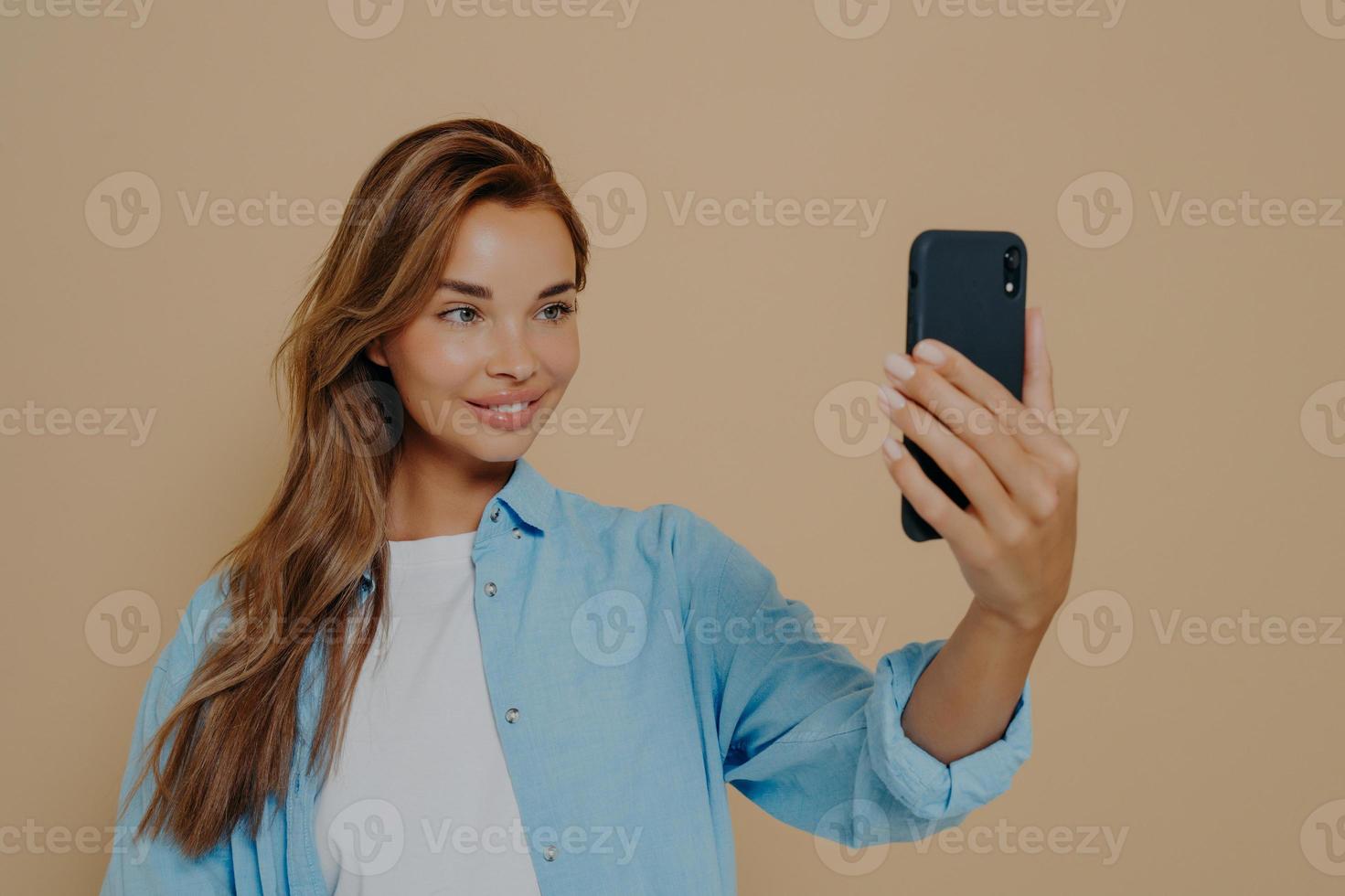 Adorable female model poses for making selfie in studio photo