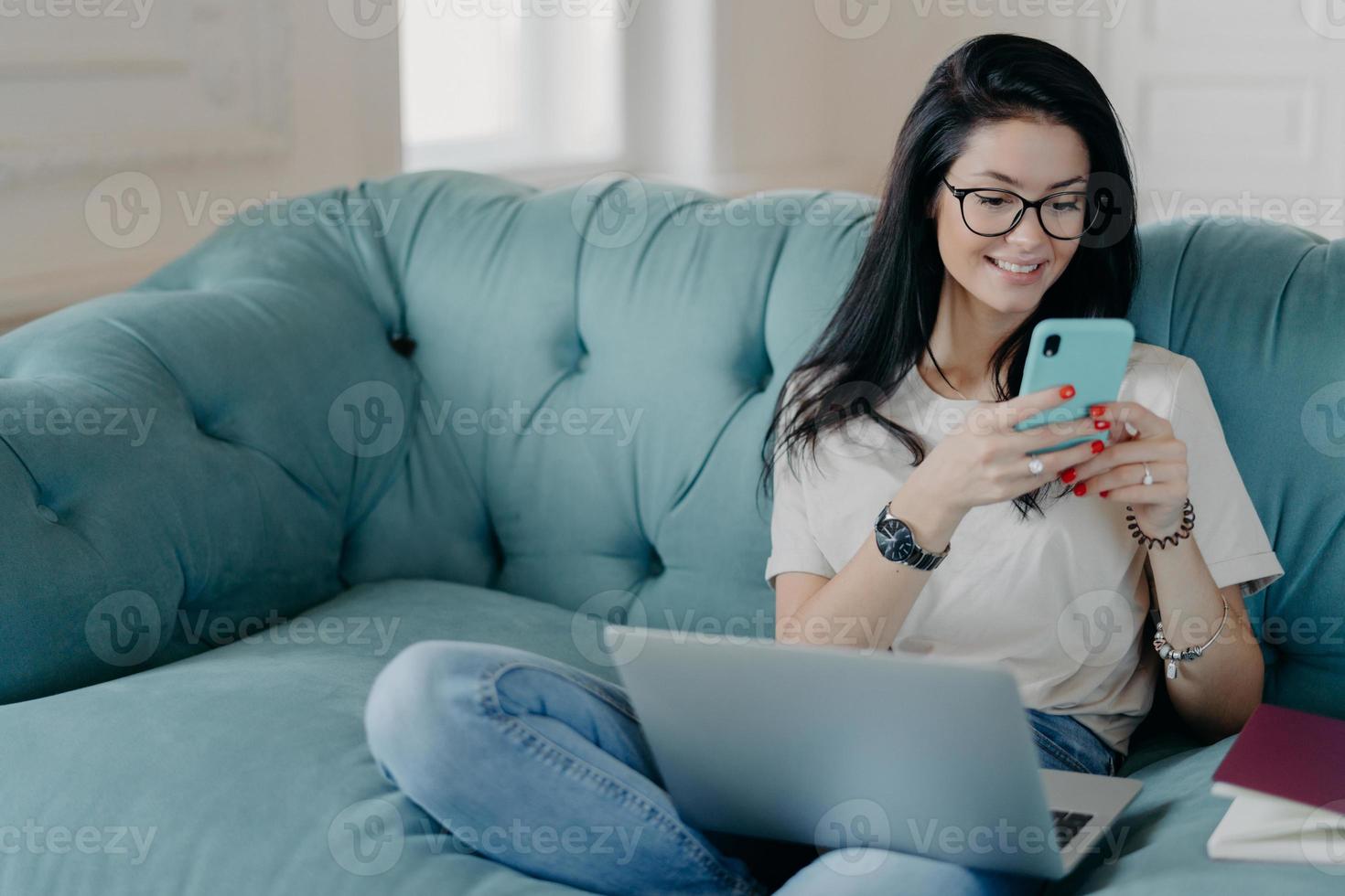 Busy female freelancer does remote job, searches information for presentation, uses modern technologies, surfs internet, sits on comfortable sofa, dressed in casual clothes, creats new publication photo