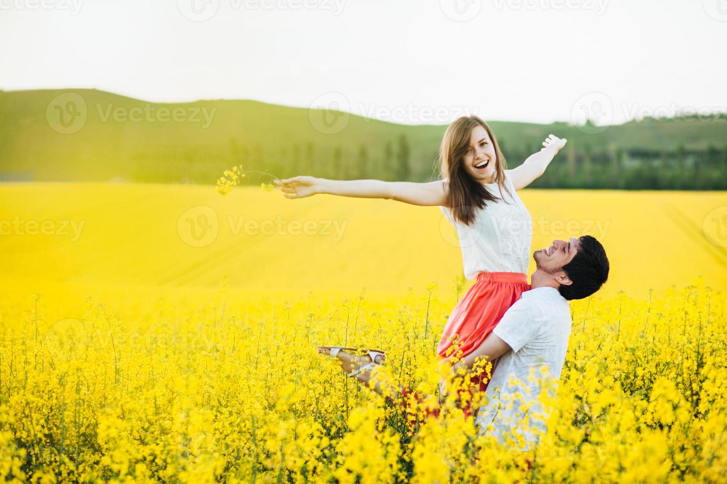 Romantic man raises his girlfriend, enjoy togetherness at beautiful yellow field, pose outdoor, have fun, smile joyfully. Couple in love spend summer holidays at nature. People and harmony concept photo