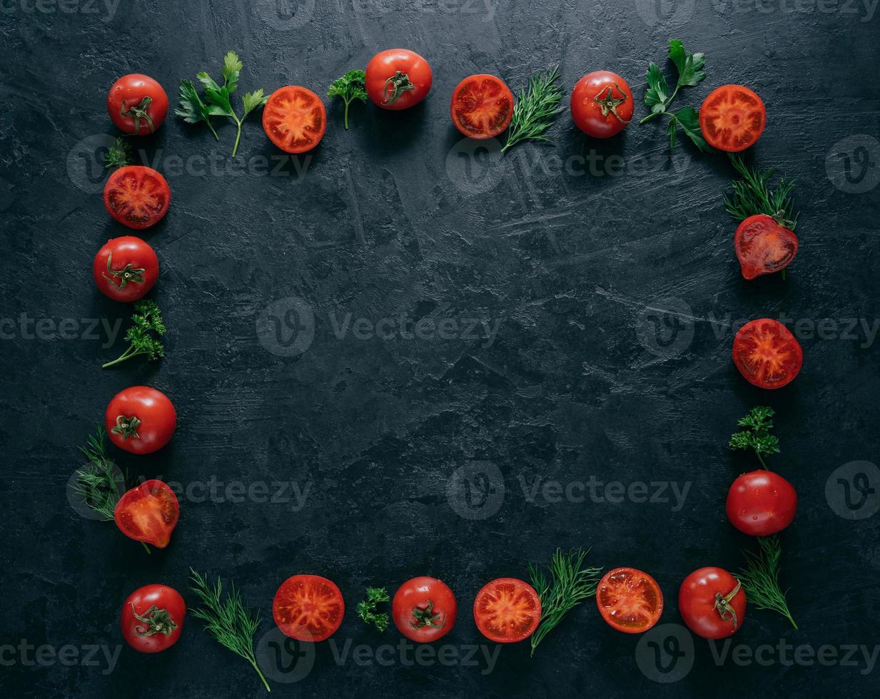 Flat lay of red ripe tomatoes lies in form of frame on dark background with green parsley and dill. Healthy vegeterian dish. Horizontal shot. Copy space for text photo