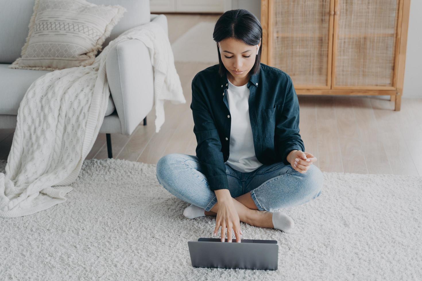 Focused woman working on laptop or learning online sitting on floor at home. E-learning, remote work photo