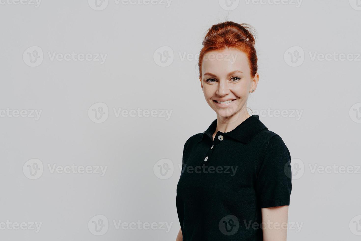 Headshot of young positive millennial red haired woman looking at camera with charming smile photo