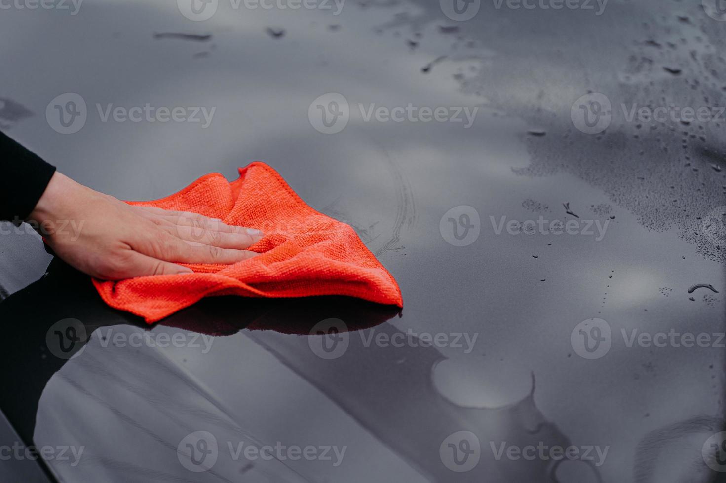 Mans hand cleans surface of black car with microfiber cloth. Maintenance and car wash concept. Professional cleaning. Selective focus photo