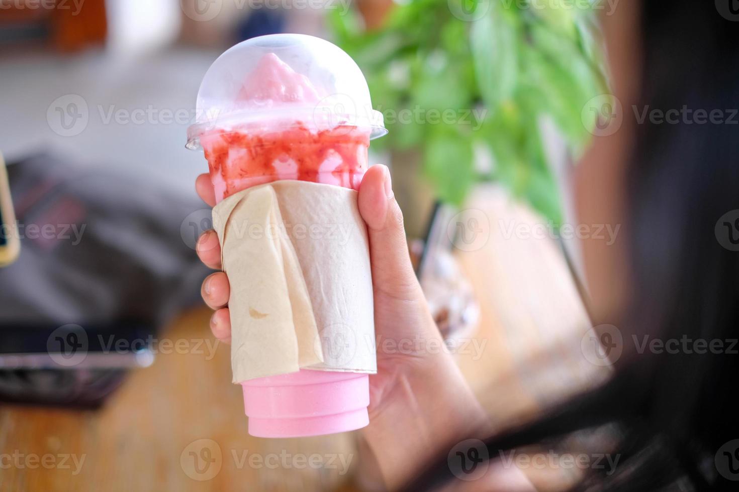 Hand holding a Strawberry smoothie milkshake mug wrapped in empty tissue paper,coffee shop, copy space photo