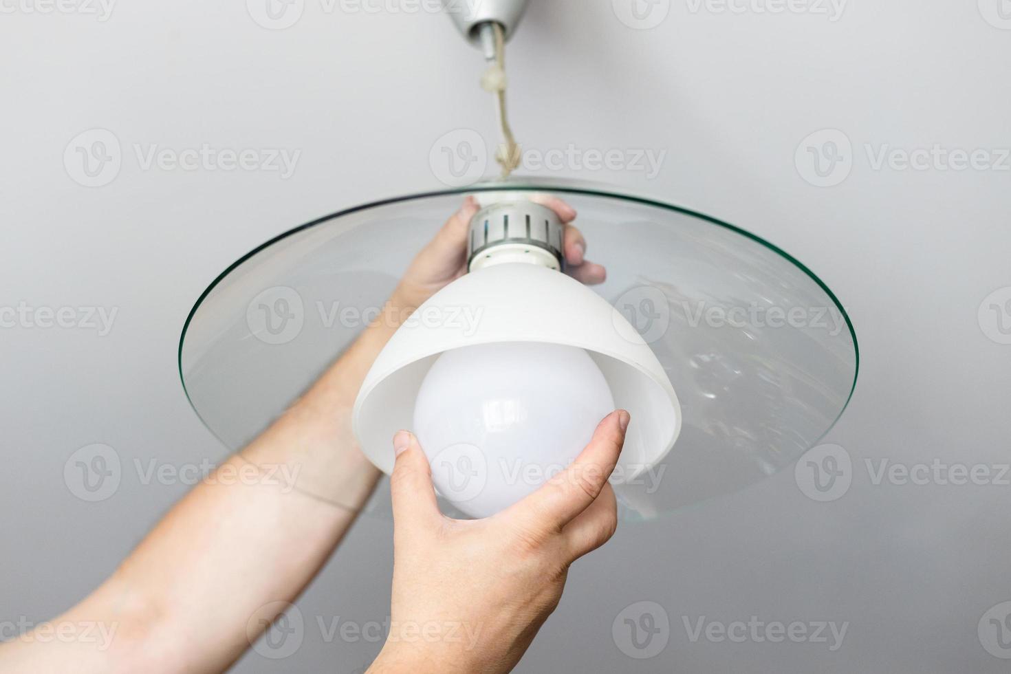 man replaces bulb of ceiling lamp photo