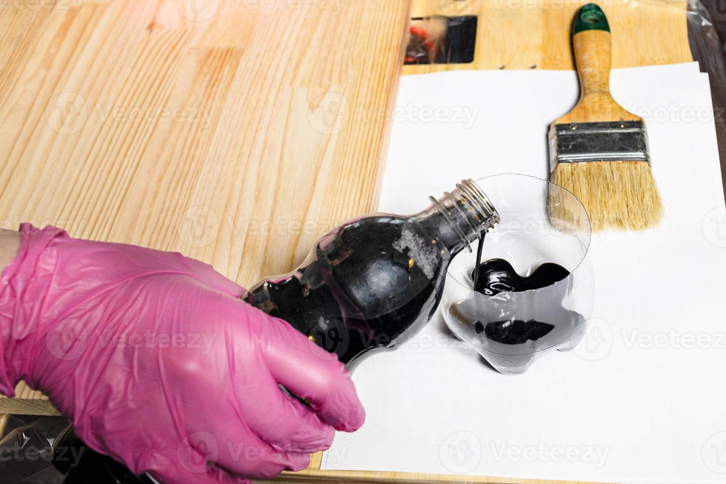 gloved hand pours wood stain from bottle into jar photo