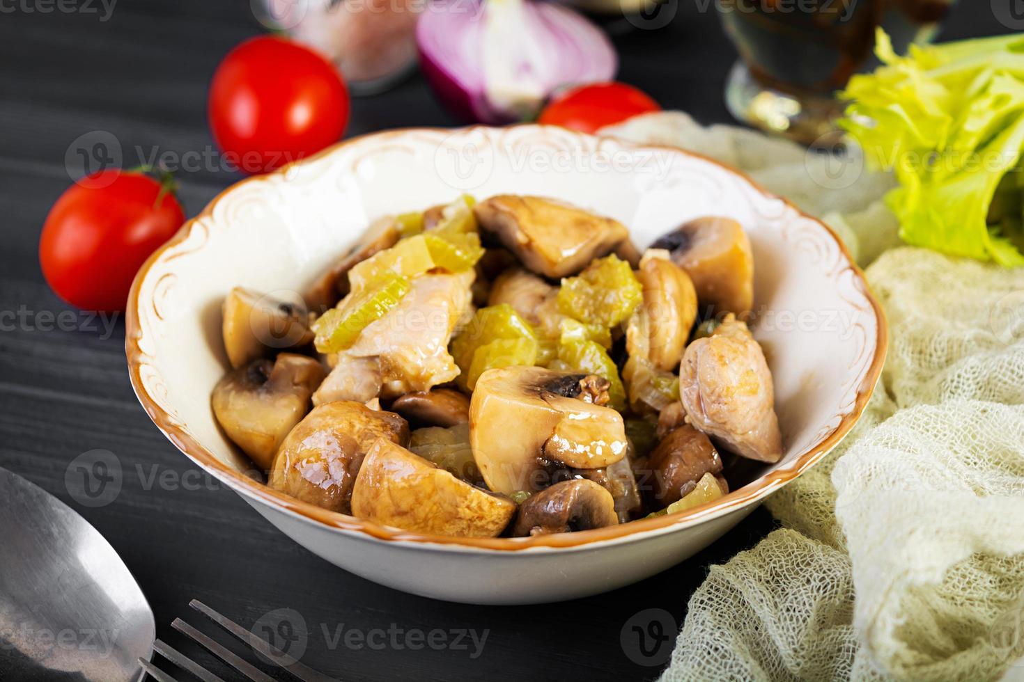 Stew chicken thighs with mushrooms, celery, onion and pepper. Stir fry chicken on wooden background photo