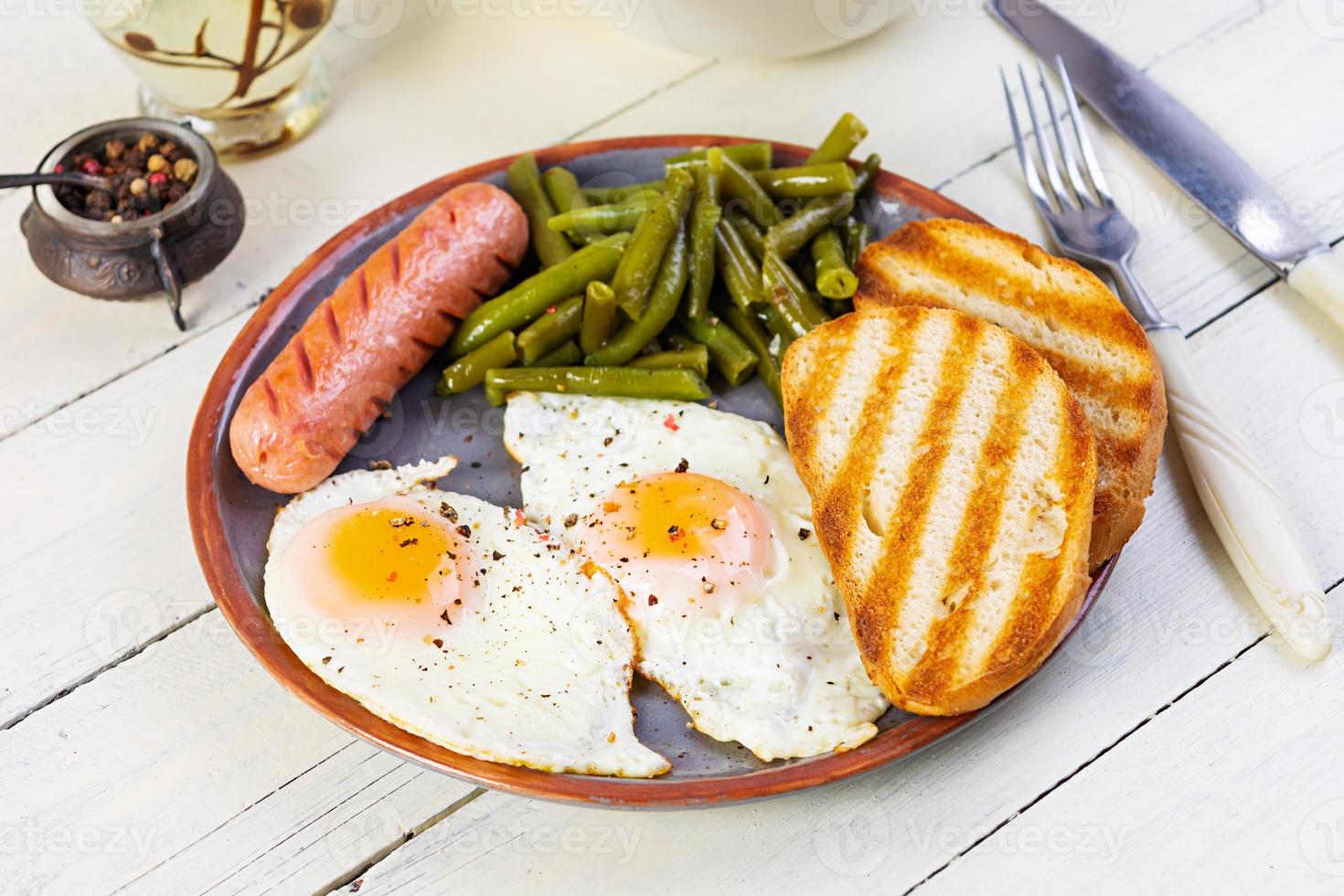 Breakfast with eggs, grilled sausage, green beans and toast on wooden background photo