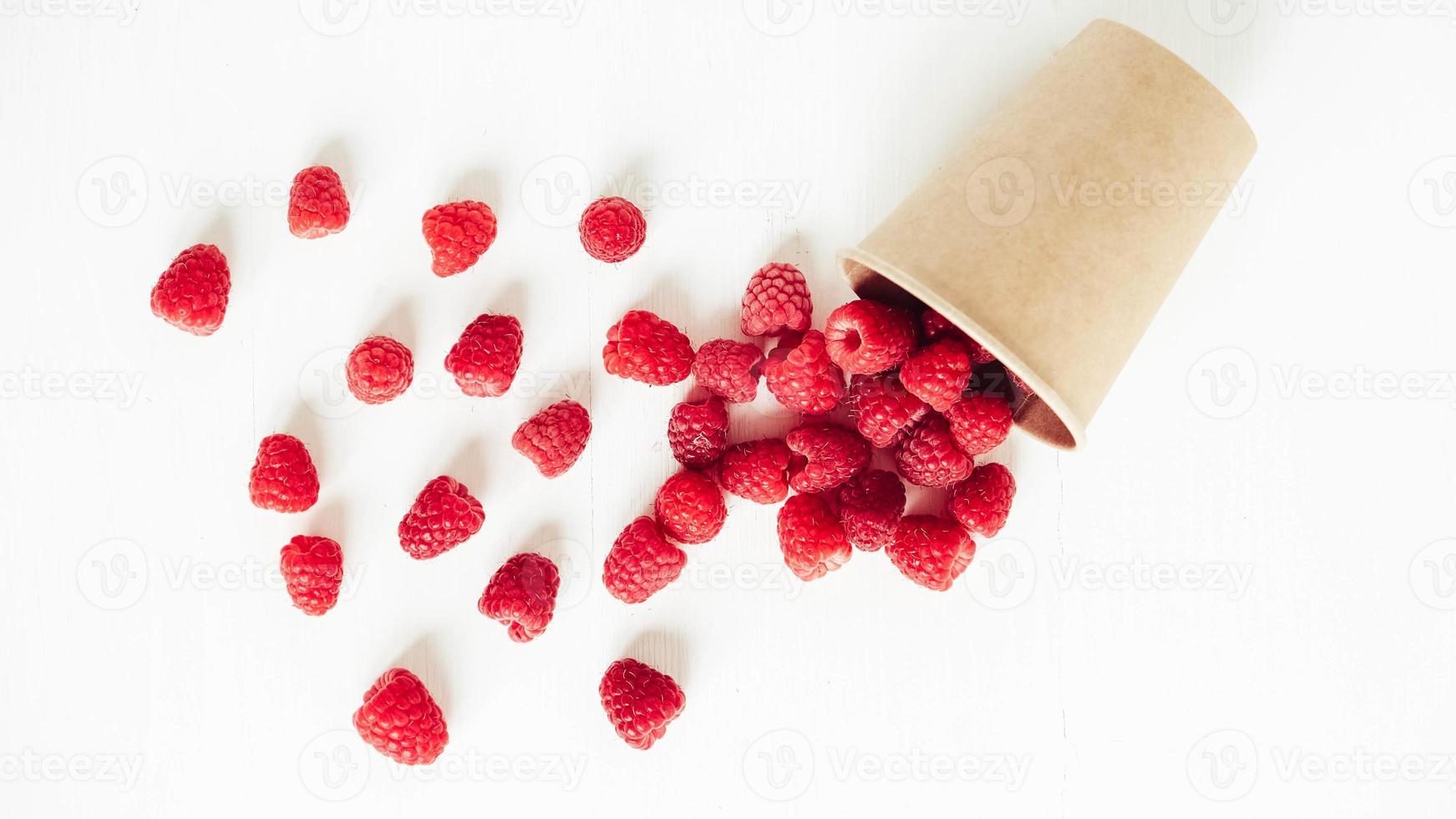 Fresh red raspberries in a paper cup on a white table background photo