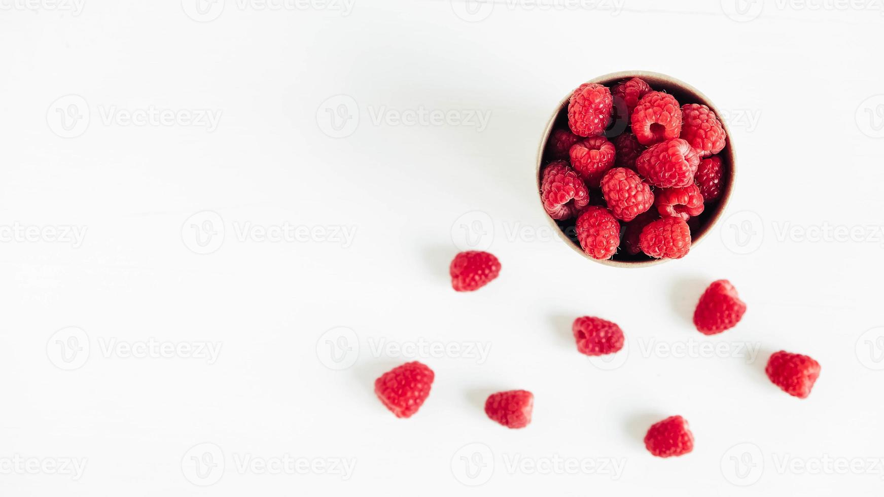 Fresh red raspberries in a paper cup on a white table background photo