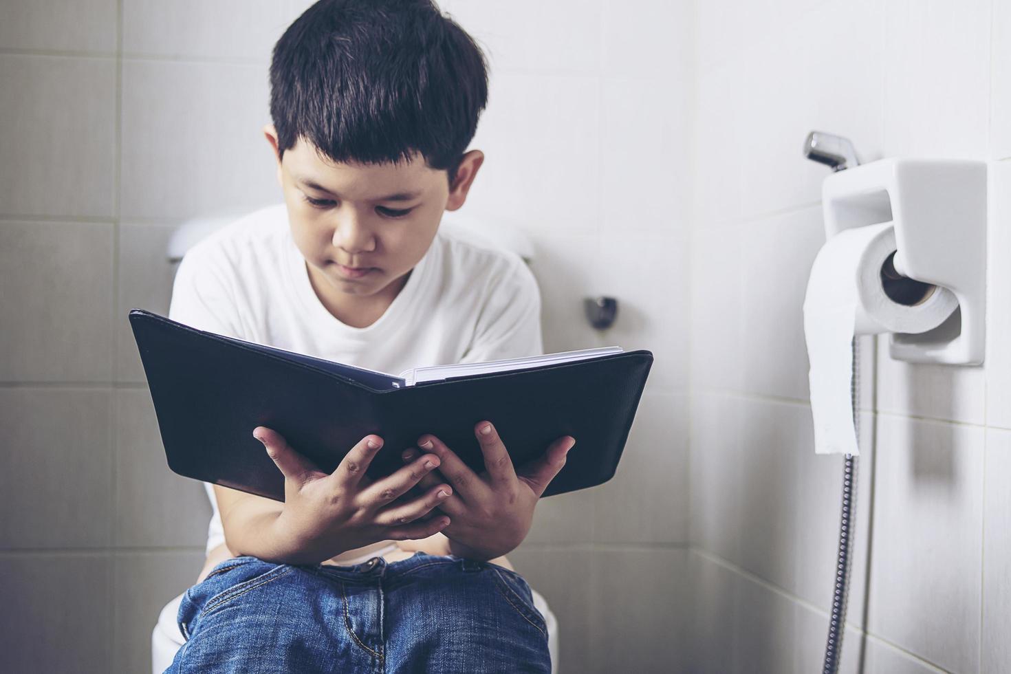 Asian boy sitting on toilet bowl while reading book - health problem concept photo