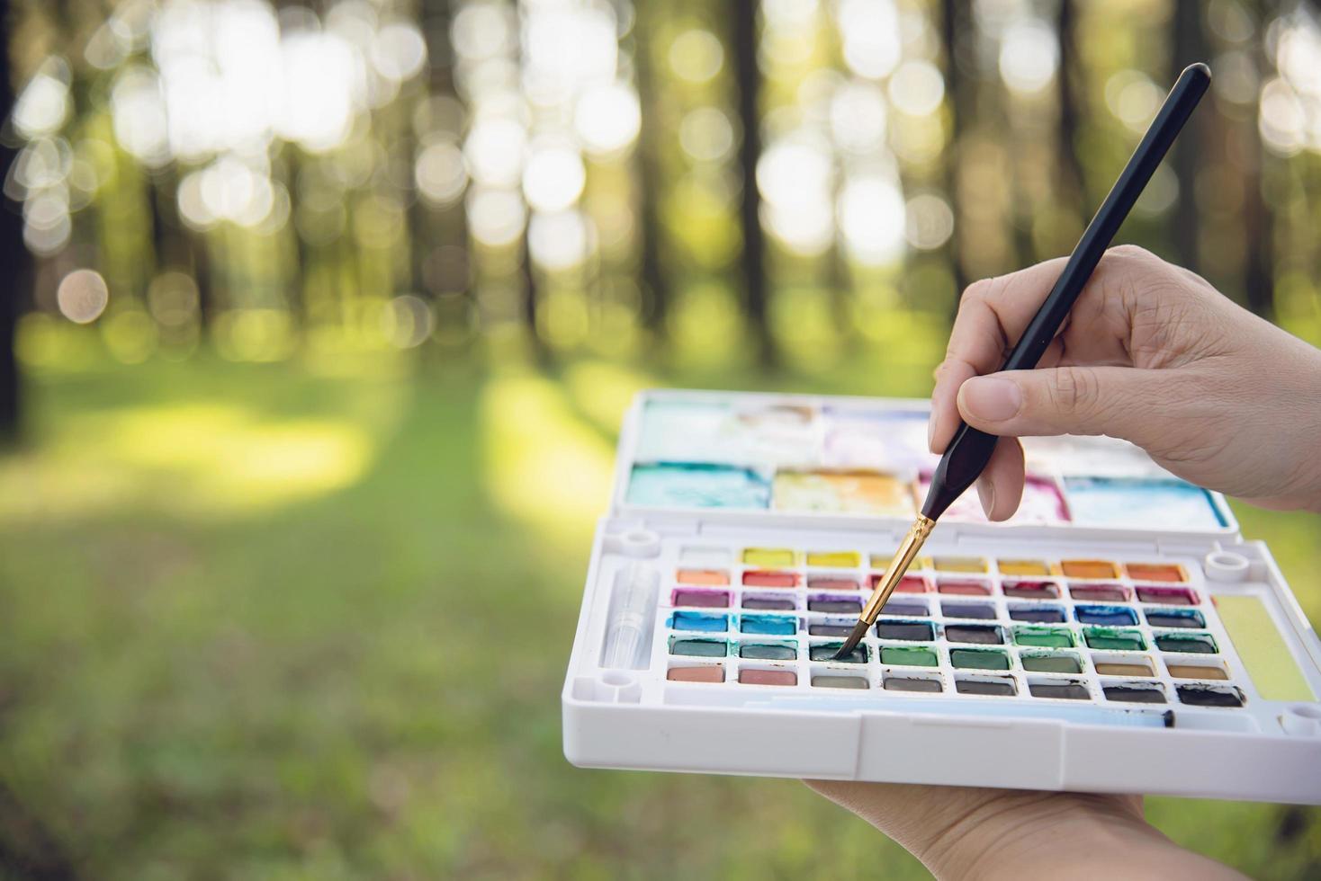 Relax woman painting water colour art work in green garden forest nature - people with creative art in nature stress reduction and meditation concept photo