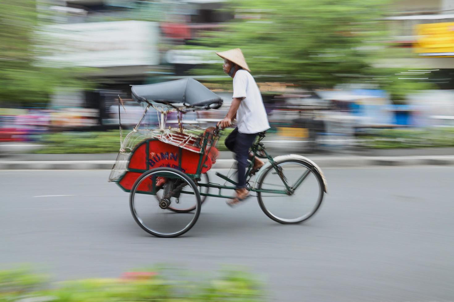 Yogyakarta, Indonesia - May 2022 Blurred motion portrait of Becak, Indonesian traditional rikshaw transport. A becak driver on his vehicle in Jalan Malioboro looking out for clients photo