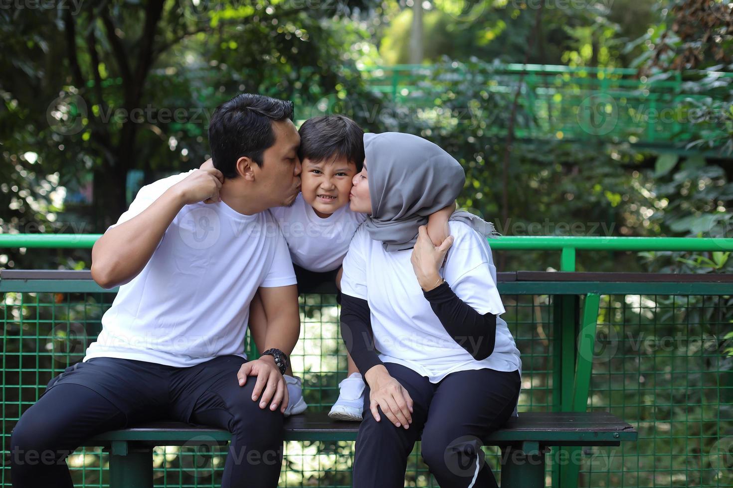 Portrait of parents and their son on the background of nature. Parents kiss their son. Happy family leisure outdoors. photo