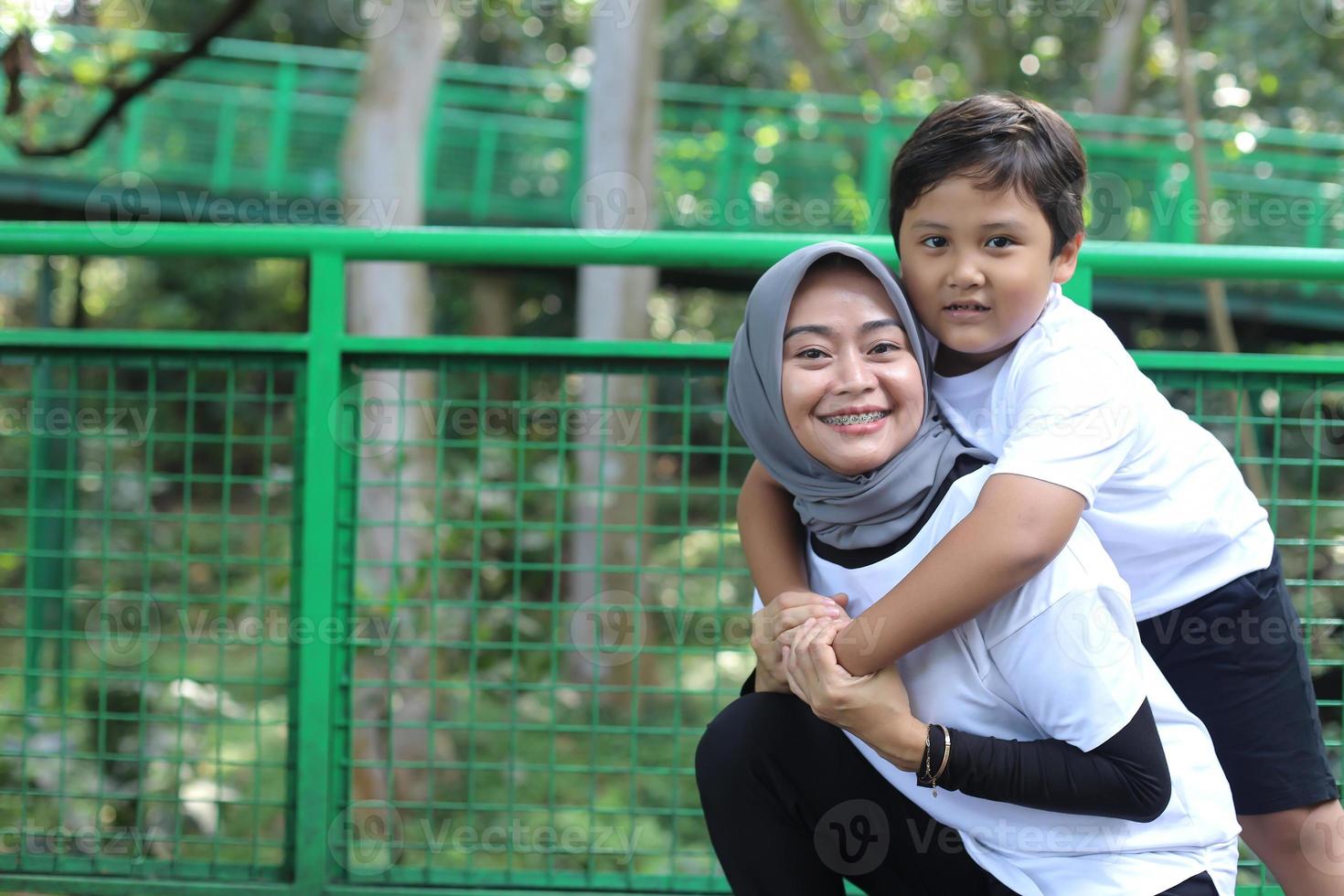 Portrait of Asian kid hugs mother from back, enjoying family time in the park. Bonding happy family concept. photo