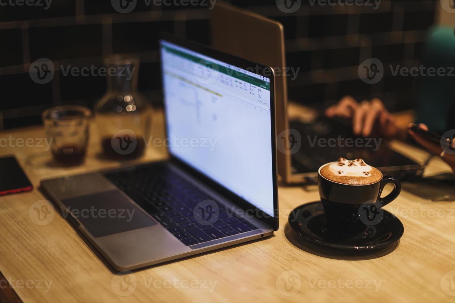 A mug of 3D latte art coffee in shape of cute cat with laptop in the background. photo