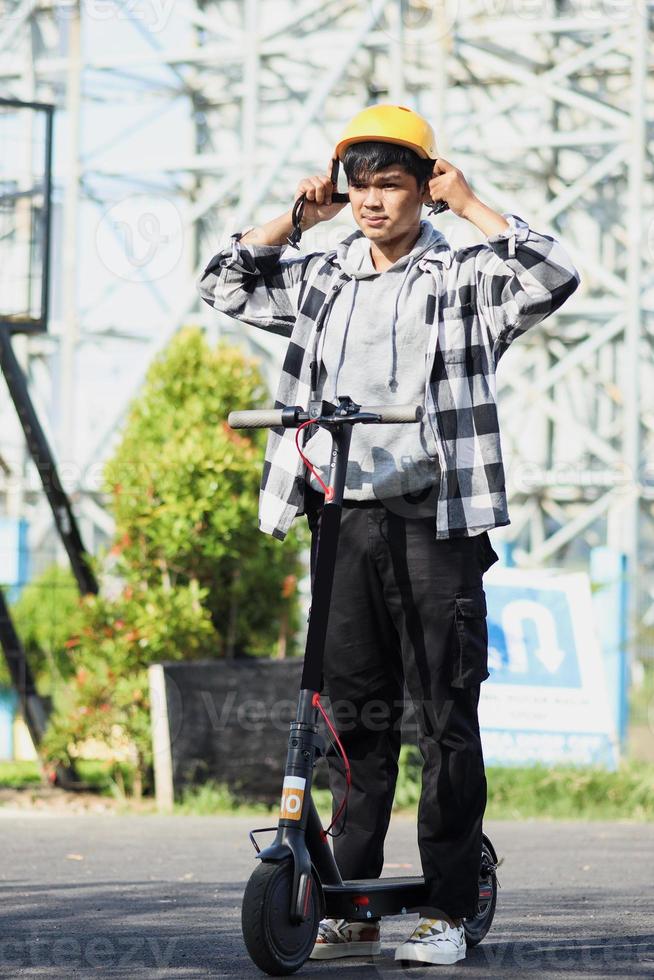 Asian man getting ready by wearing safety helmet before driving an electric scooter. Modern and ecological transportation concept. photo