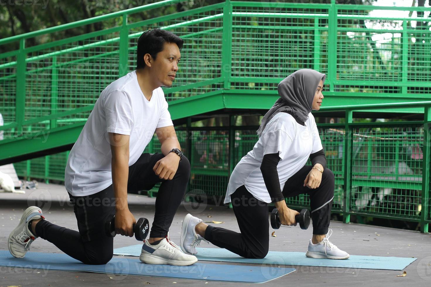 Happy Asian couple working out together with dumbbells in outdoor. Health and fitness concept. photo