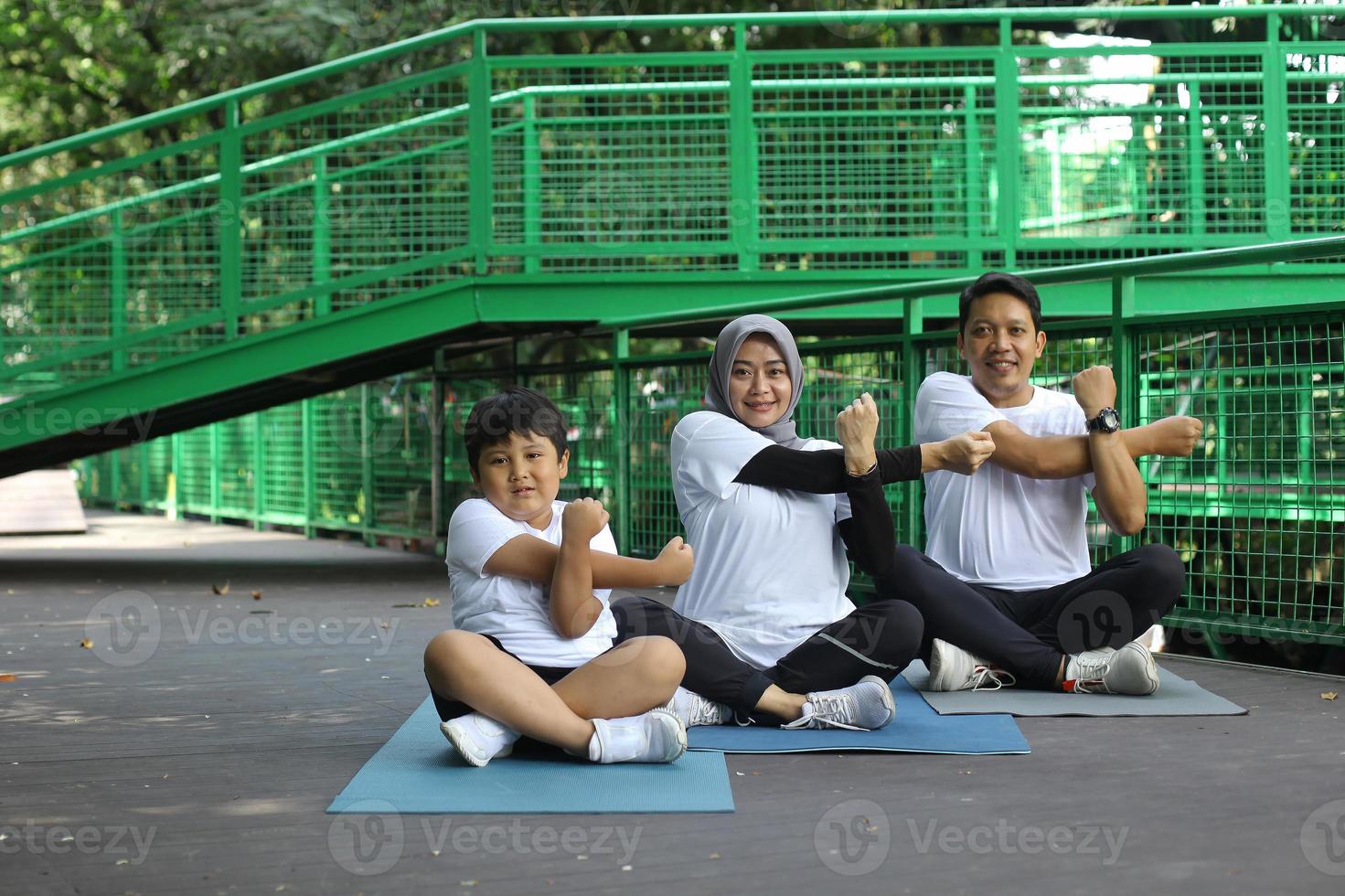 Asian young mother and father practicing yoga and stretching hand with son  at the park. Family sport concept. photo