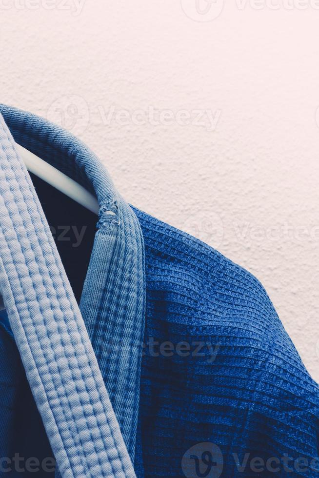 Close up on brazilian jiu jitsu or judo blue kimono uniform hanging next to a wall photo