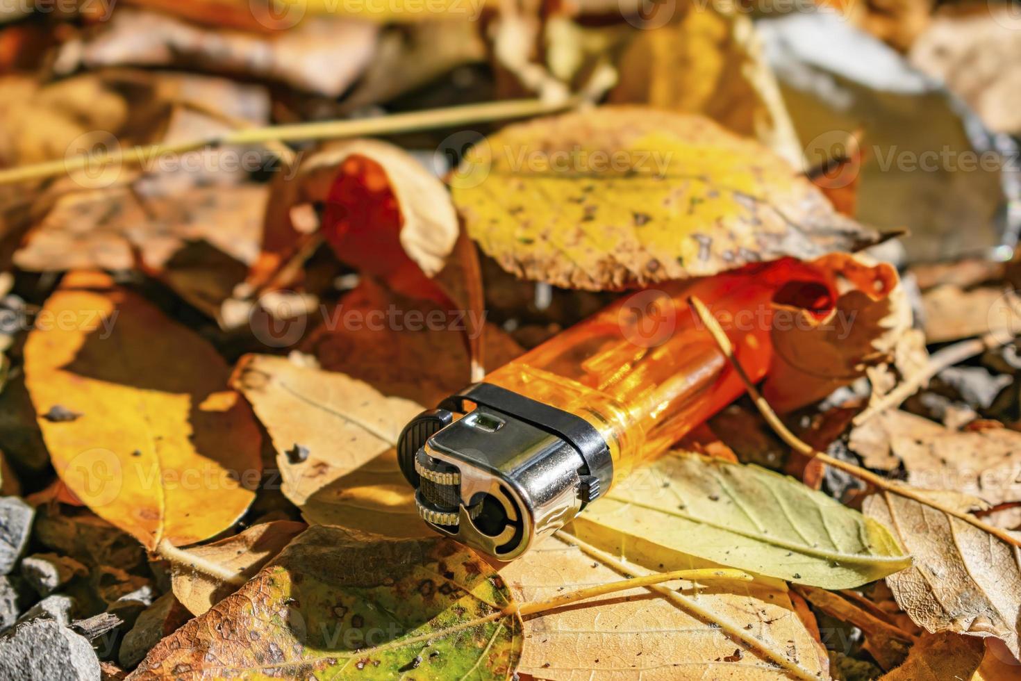 An old orange lighter is thrown into the autumn foliage photo