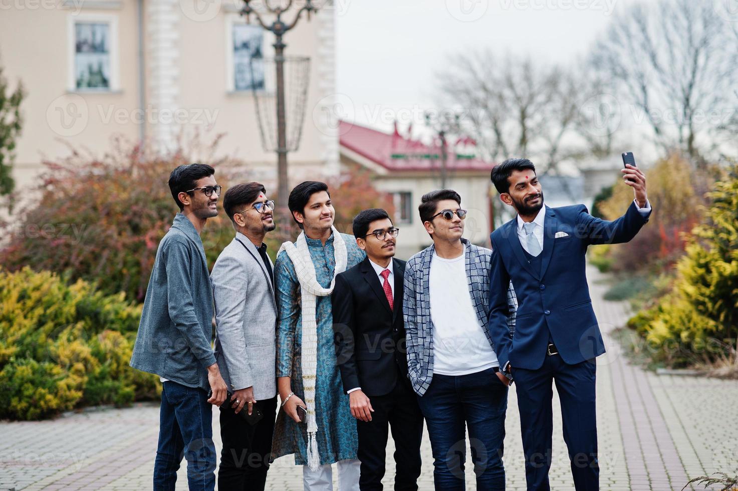 Group of six south asian indian mans in traditional, casual and business wear standing and making selfie at mobile phone together. photo