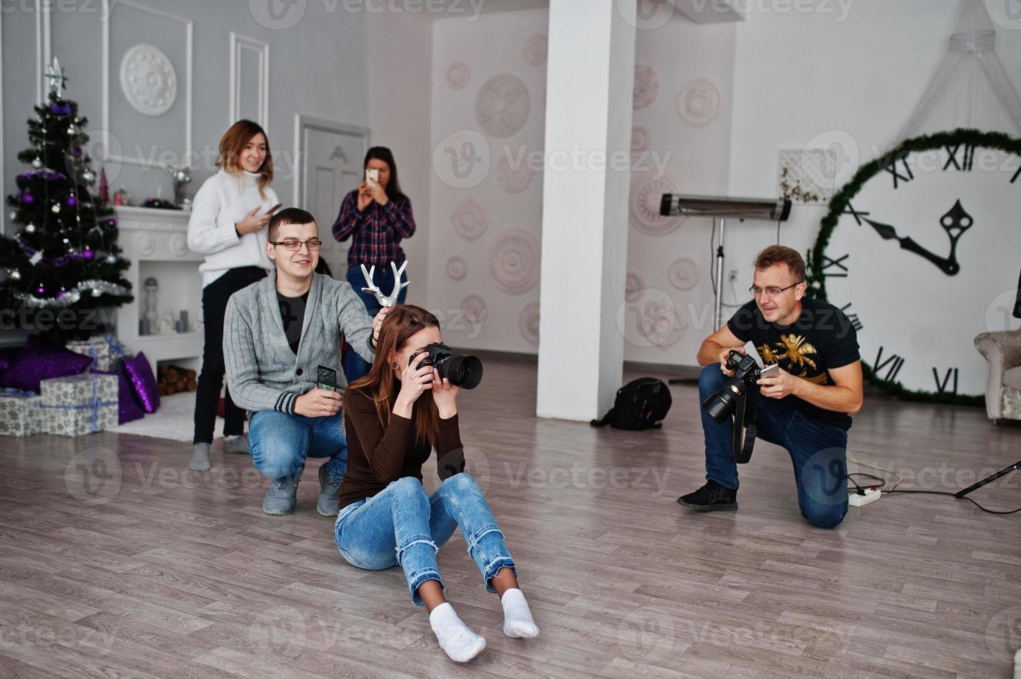 The team of two photographers shooting on studio behind another three workers. Professional photographer on work. One of them joking and holds horns over head. photo
