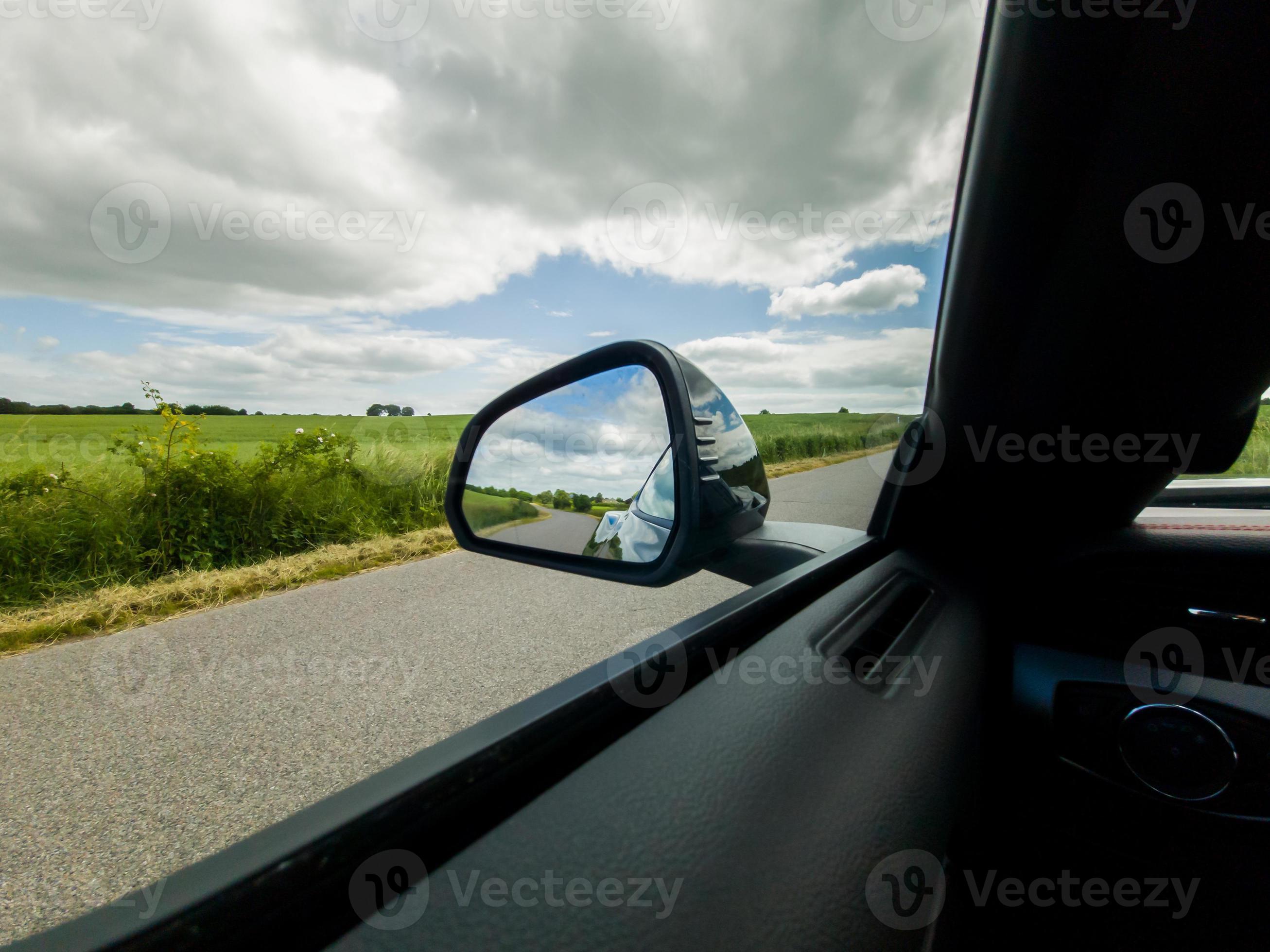 View into the side mirror of a black sports car while driving. 10252675