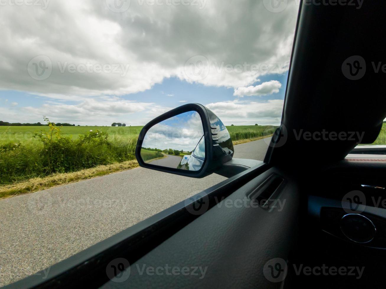 View into the side mirror of a black sports car while driving. photo