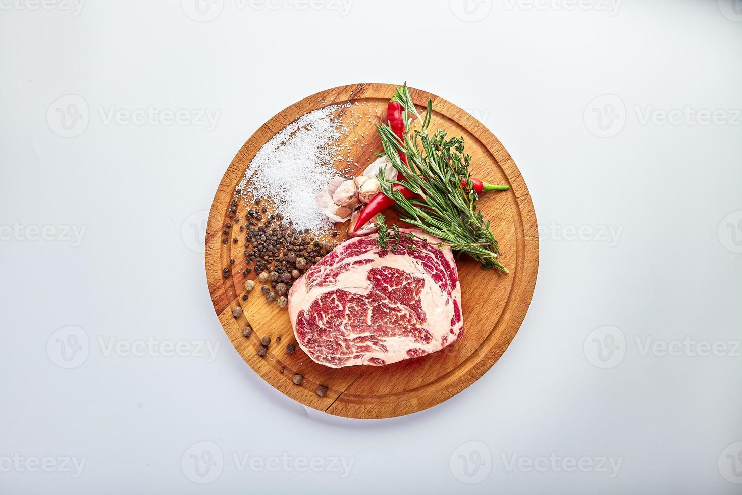 bistec de chuletón en la tabla del carnicero con romero, pimienta y sal en una mesa de madera, preparado para cocinar. foto