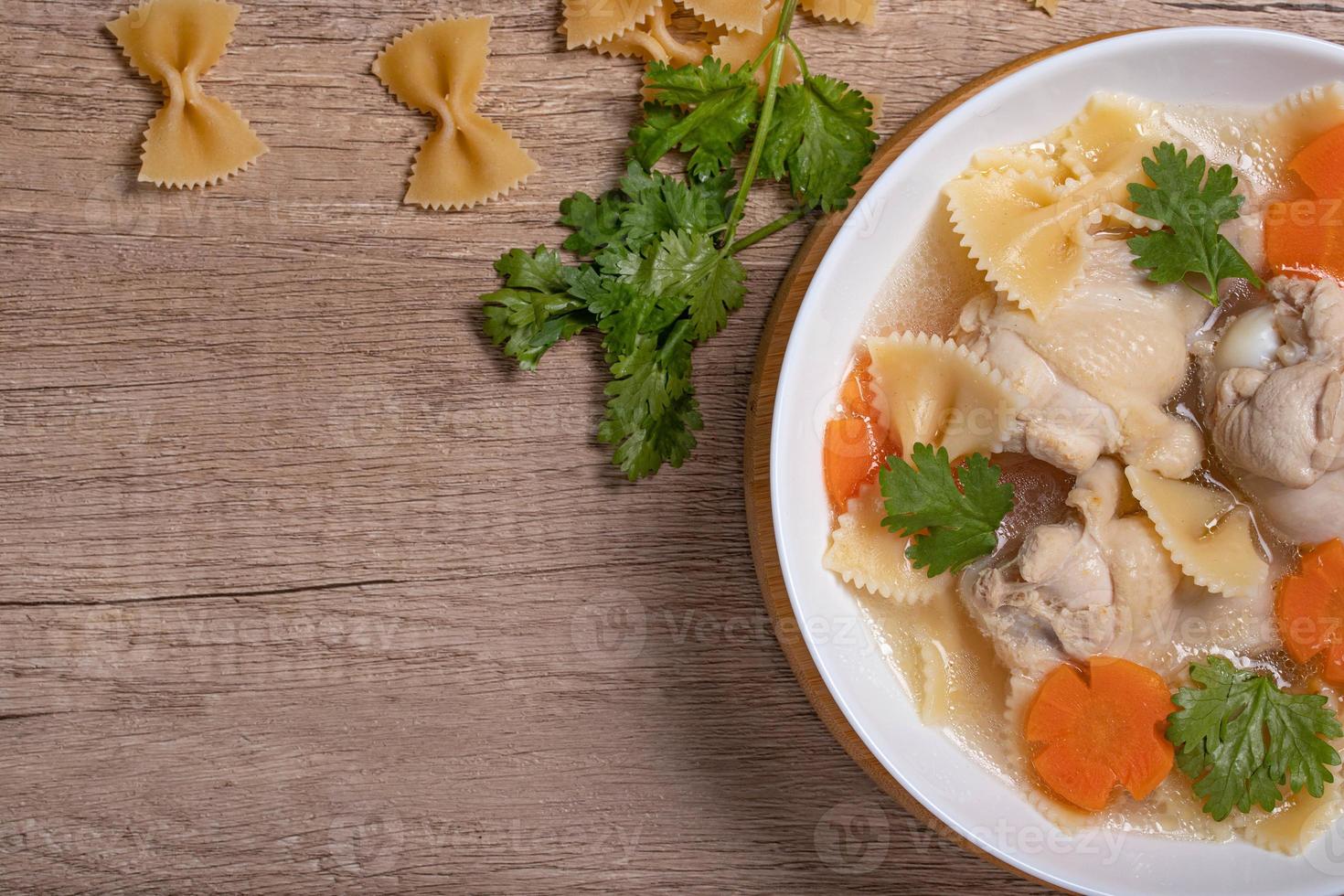 Macaroni soup with chicken thighs in clear broth with carrots.on an rustic old wood background. photo