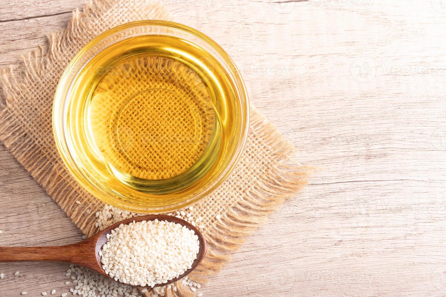 sesame oil in a bowl and white sesame seeds on wooden background photo