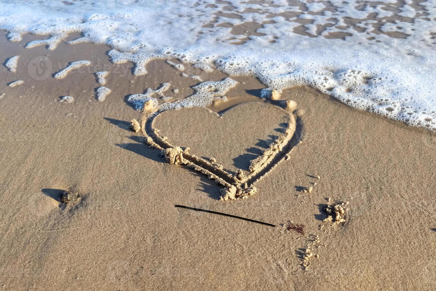 A beautiful heart shape painted into the sand of a baltic sea beach with some water waves. photo